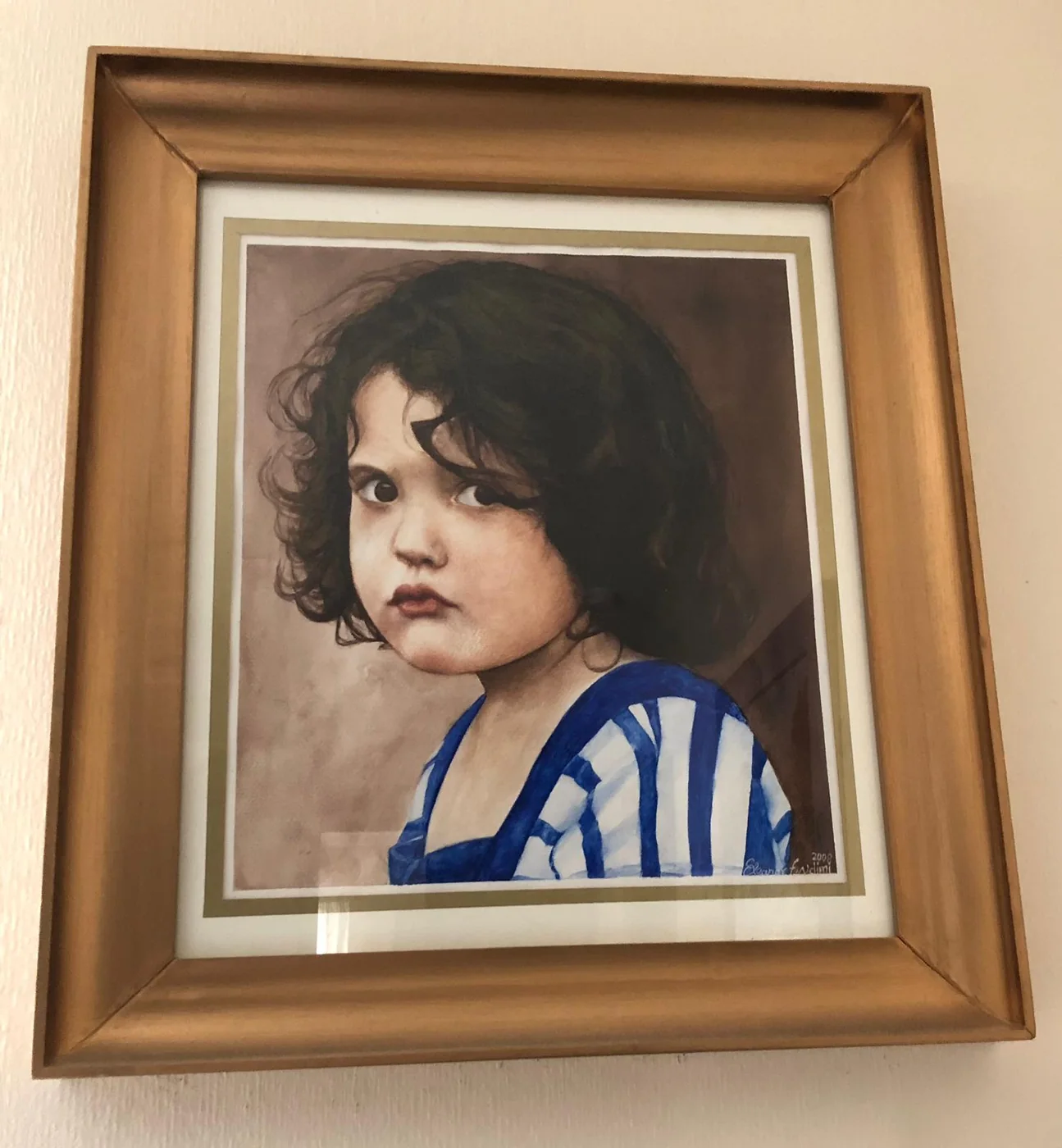 A framed portrait of a young child with dark curly hair, in a blue and white striped top, looking over one shoulder against a soft brown ground.